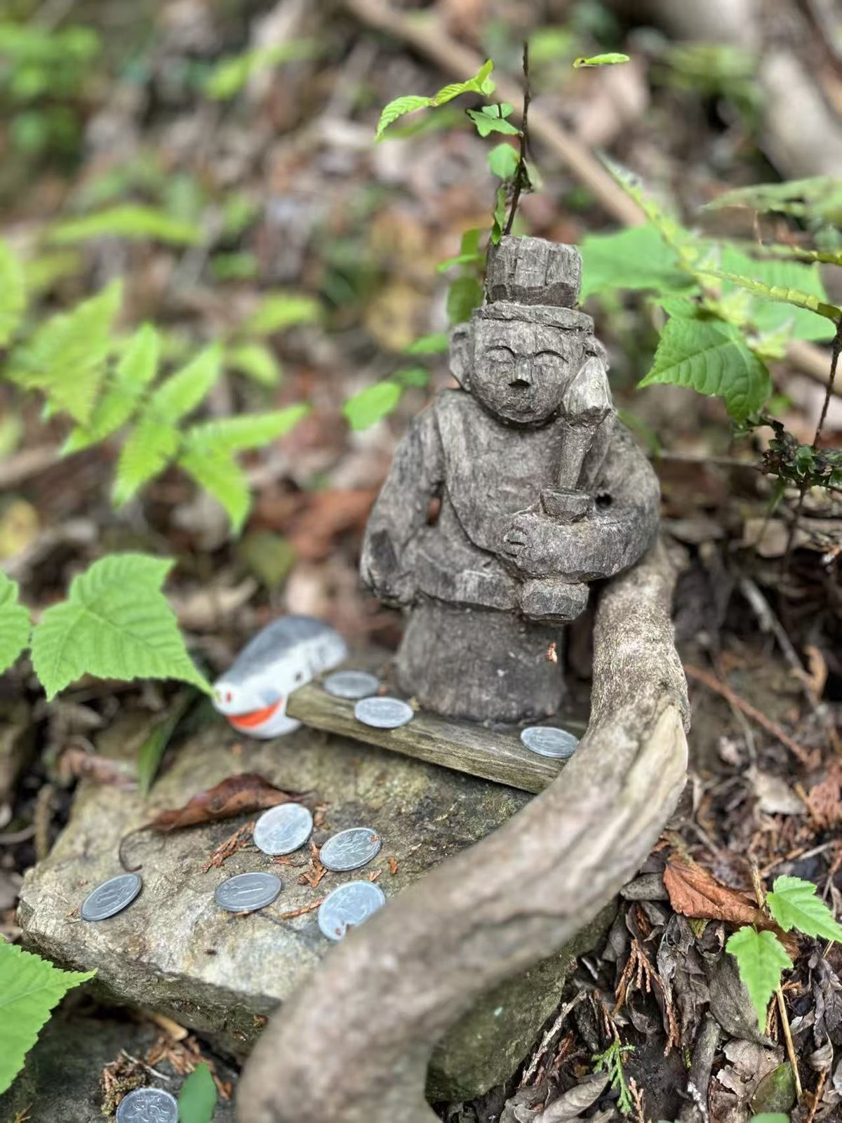 日本山间小径旁的木雕山神像,前方石台上摆着香客供奉的硬币
