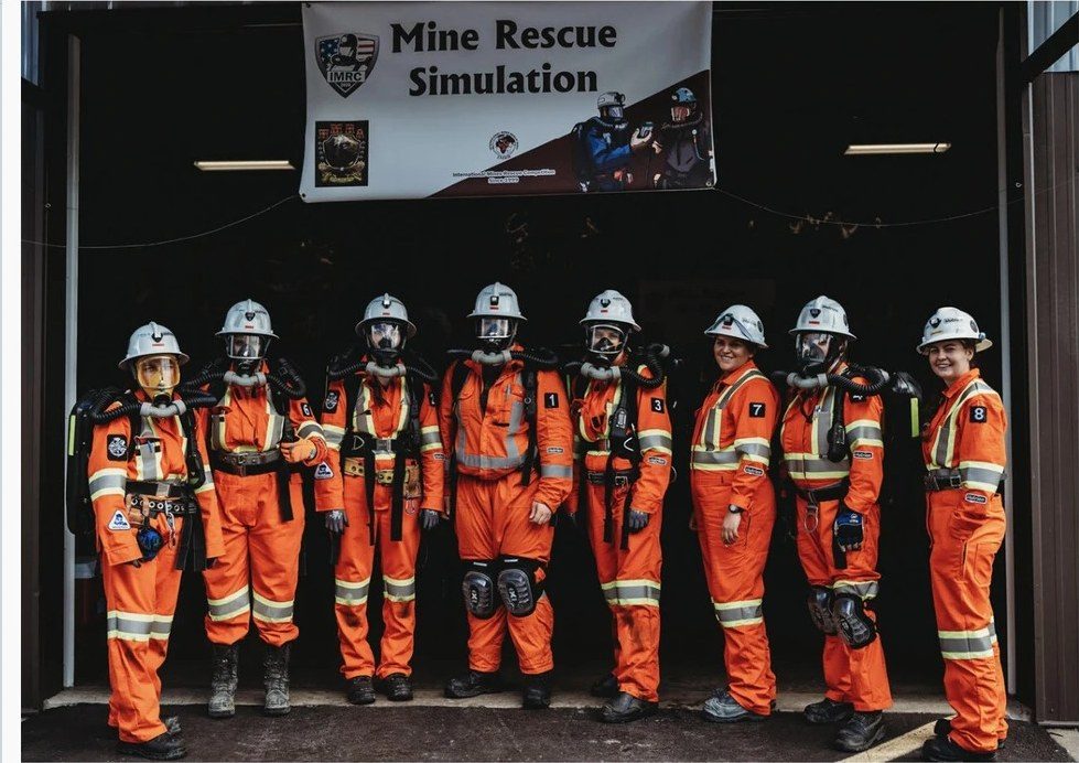 璞玉全女子救援队身穿橙色救援服,站在写着 Mine Rescue Simulation 的横幅下